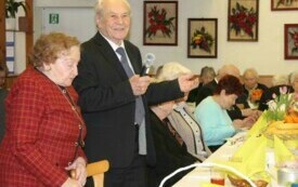 Na zdjęciu osoby w odświętnych strojach, przed stołami ze świątecznym nakryciem