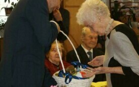 Na zdjęciu osoby w odświętnych strojach, przed stołami ze świątecznym nakryciem