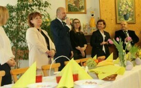 Na zdjęciu osoby w odświętnych strojach, przed stołami ze świątecznym nakryciem