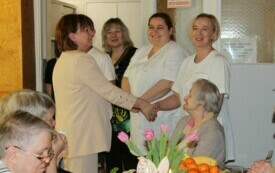 Na zdjęciu osoby w odświętnych strojach, przed stołami ze świątecznym nakryciem