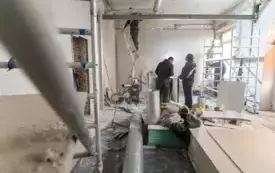 Zdjęcie przedstawia szerokie ujęcie remontowanego pomieszczenia. Widać skute ściany, narzędzia oraz pracownik&oacute;w budowlanych