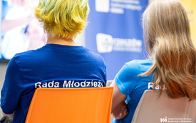 Na zdjęciu grupa os&oacute;b w trakcie spotkania w pomieszczeniu z projektorem i plakatami