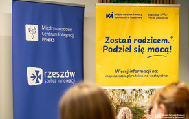 Na zdjęciu grupa os&oacute;b w trakcie spotkania w pomieszczeniu z projektorem i plakatami
