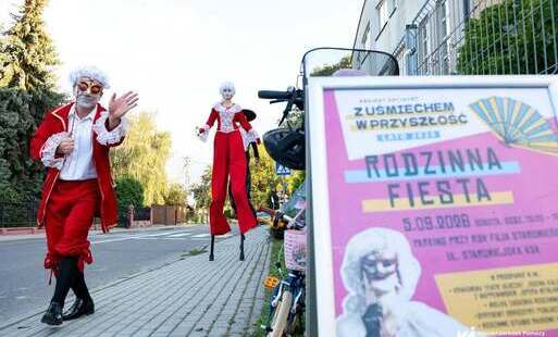 Na zdjęciu aktorzy teatru ulicznego na drodze, w pierwszym planie plakat wydarzenia