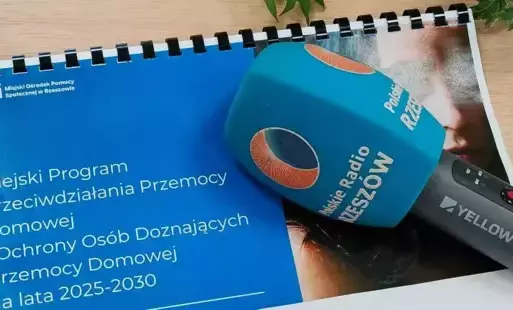 Na zdjęciu mikrofon z logo polskie Radio Rzeszów a niebieskim pliku kartek z napisem 'Miejski Program Przeciwdziałania Przemocy Domowej i Ochrony Osób Doznających Przemocy Domowej na lata 2025-2030