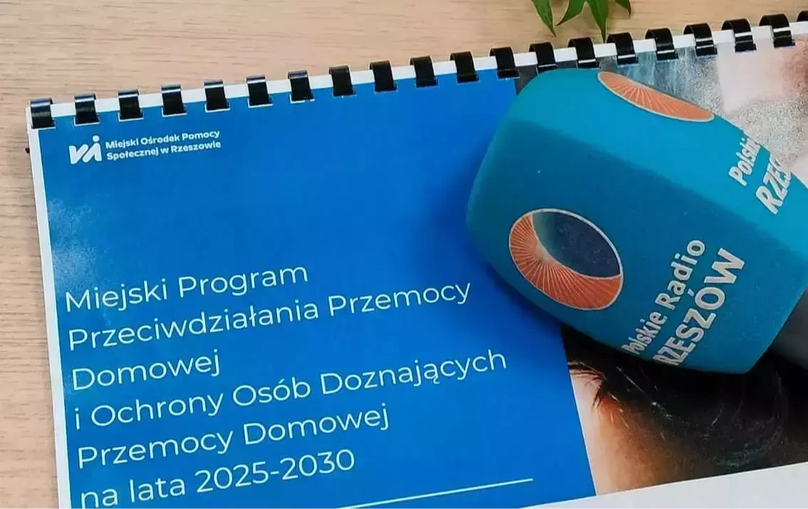 Na zdjęciu mikrofon z logo polskie Radio Rzeszów a niebieskim pliku kartek z napisem 'Miejski Program Przeciwdziałania Przemocy Domowej i Ochrony Osób Doznających Przemocy Domowej na lata 2025-2030
